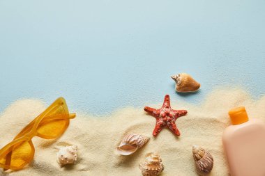 kum ve deniz kabukları ile mavi arka plan üzerinde güneş gözlüğü yakınında şişe güneş kremi losyon üst görünümü