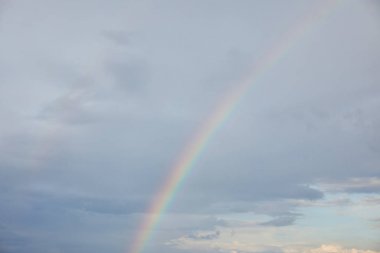 rainbow on blue sky background with clouds and sunlight clipart