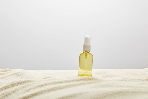 suntan oil in transparent yellow spray bottle in sand on grey background
