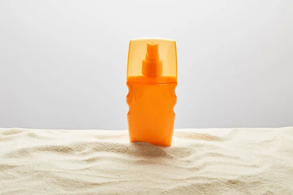灰色の背景にテクスチャード砂のオレンジ色のボトルの日焼け止め — ストック写真
