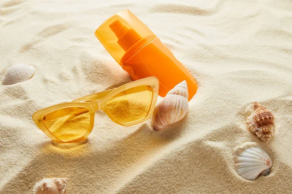 Κίτρινα Γυαλιά Ηλίου Και Αντηλιακό Πορτοκαλί Μπουκάλι Στην Άμμο Κοχύλια — Φωτογραφία Αρχείου