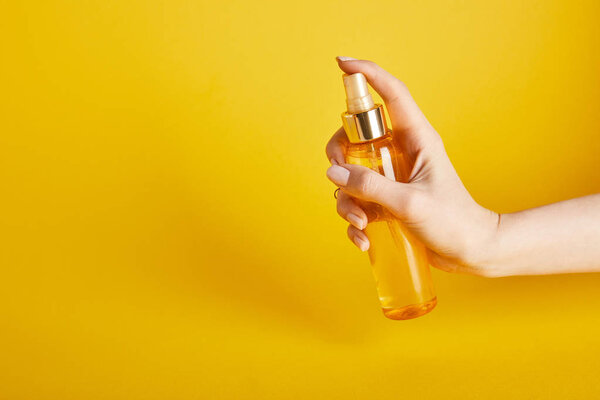 cropped view of woman holding suntan oil in spray bottle on yellow background