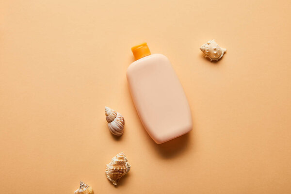 top view of sunscreen in bottle near seashells on beige background