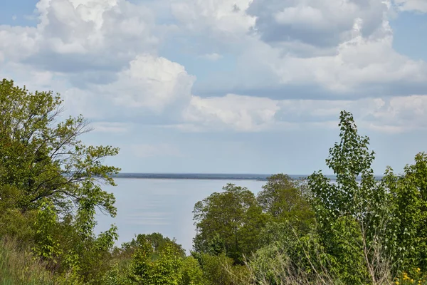 Landscape with green leafy trees, river and peaceful sky