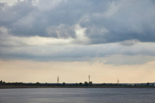 blue clouds, river and coast with electric poles on sunset background