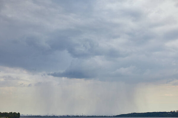 overcast view of blue clouds and rain upon forest coast