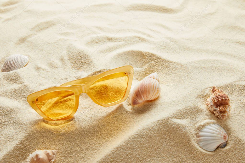 yellow stylish sunglasses on sand with seashells
