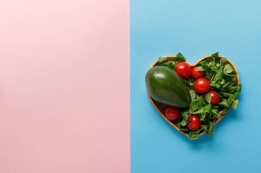 pembe ve mavi arka planda kalp şeklinde kase taze yeşil sebze salatası üst görünümü