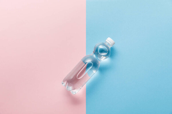 top view of bottle with water on blue and pink background