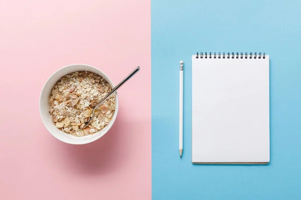 青とピンクの背景に鉛筆とボウルと空白のノートブックで朝食シリアルのトップビュー — ストック写真