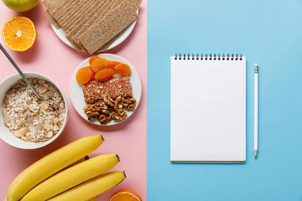 青い背景にピンクと空白のノートブックに新鮮な果物 クリスプブレッドと朝食シリアルのトップビュー — ストック写真