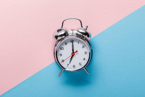 top view of classic silver alarm clock on pink and blue background