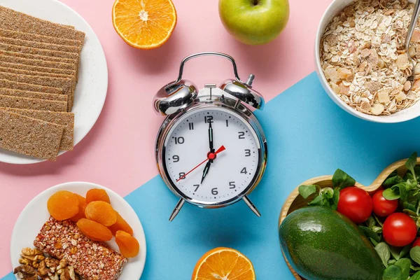 青とピンクの背景においしいダイエット食品と銀目覚まし時計のトップビュー — ストック写真