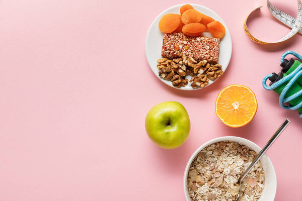 top view of fresh diet food, measuring tape, skipping rope on pink background with copy space