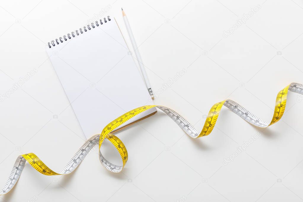 top view of measuring tape, blank notebook with pencil on white background 