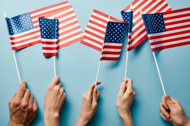 mavi arka plan üzerinde Amerikan bayrakları tutan insanların kısmi görünümü