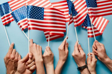 mavi arka plan üzerinde sopalar üzerinde Amerikan bayrakları tutan insanların kırpılmış görünümü 
