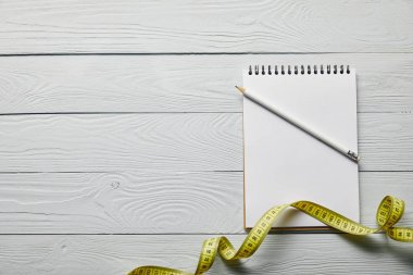 sarı ölçüm bandı üst görünümü, ahşap beyaz arka plan üzerinde kopya alanı ve kalem ile boş defter 