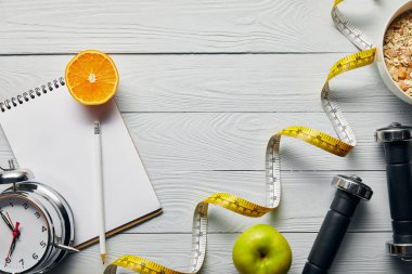 ölçüm bandı üst görünümü, elma, portakal, dizüstü bilgisayar, dambıl, çalar saat ve kopya alanı ile ahşap beyaz arka plan üzerinde kalem yakın kase kahvaltılık gevrek