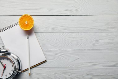 kopya alanı ile ahşap beyaz arka plan üzerinde çalar saat yakın turuncu yarım, defter ve kalem üst görünümü