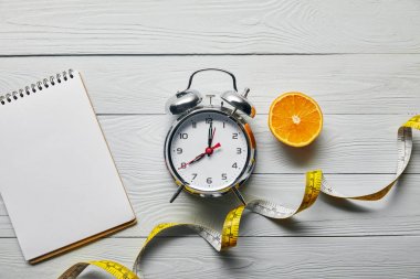 turuncu yarım üst görünümü, boş dizüstü bilgisayar ve ahşap beyaz arka plan üzerinde çalar saat yakın ölçüm bandı 