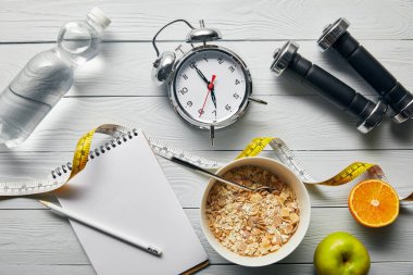 çalar saat üst görünümü, halter, su, kalem ile defter, kase kahvaltılık gevrek, ahşap beyaz arka plan üzerinde bant ölçme yakın elma ve portakal