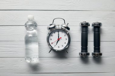 düz gümüş çalar saat, su şişesi ve ahşap beyaz arka plan üzerinde dambıl ile yatıyordu 