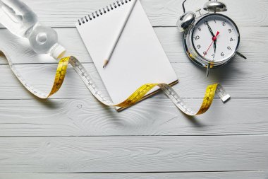 kopyalama alanı ile ahşap beyaz arka plan üzerinde ölçüm bandı, boş dizüstü bilgisayar, su ve çalar saat üst görünümü