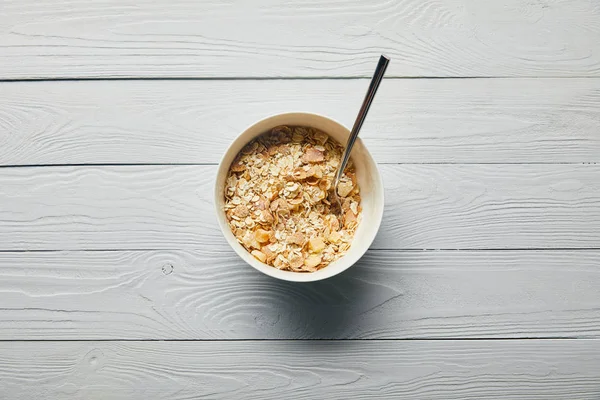 top view of breakfast cereal in bowl with spoon on wooden white background