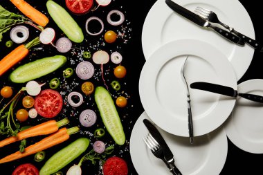 siyah üzerinde izole dilimlenmiş sebzelerin yakınında yuvarlak plakalar ve çatal bıçak üst görünümü