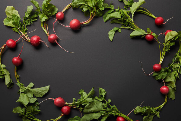 top view of whole nutritious tasty radish with green leaves on black background with copy space