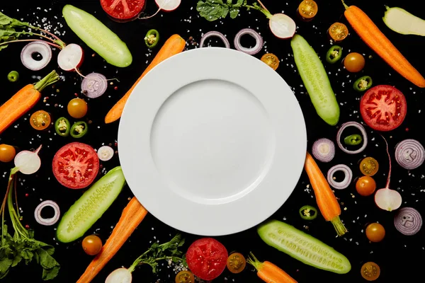 黒に分離された野菜パターンの背景にコピースペースで空の丸いプレートの上面図 — ストック写真