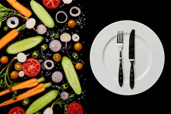 黒に分離された野菜のスライスの近くに銀のカトラリーと丸いプレートのトップビュー — ストック写真