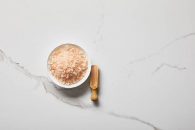 top view of sea salt in bowl near wooden spatula on marble table clipart