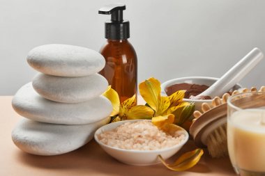 gri izole bej yüzeyüzerinde spa kozmetik, taş, masaj fırçası, mum ve sarı çiçekler seçici odak