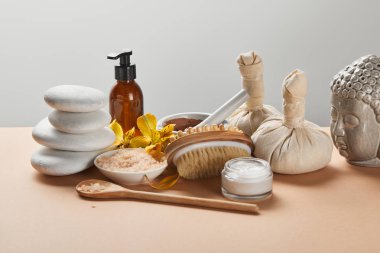 gri izole bej yüzeyinde spa kozmetik, taşlar, masaj fırçası, mum, Buda heykelcik ve sarı çiçekler