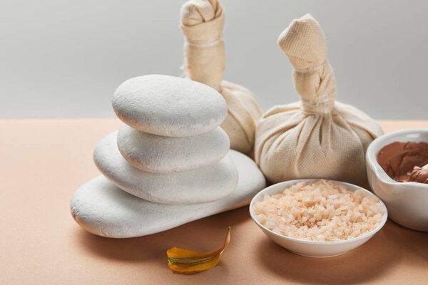 sea salt, clay, stones and yellow flower petal on beige surface isolated on grey