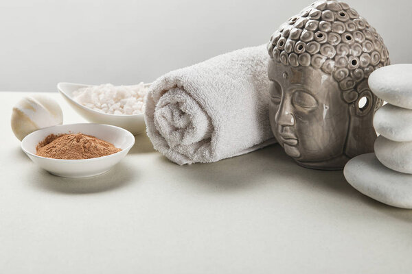 sea salt and clay powder in bowls, cotton towel, stones, bath bomb and Buddha figurine on white table isolated on grey