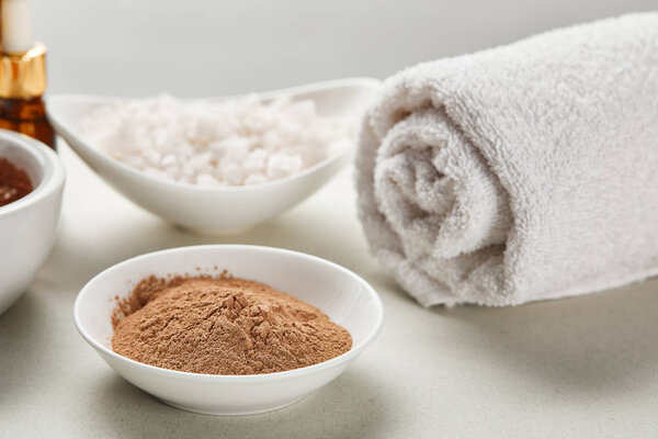 selective focus of clay powder and sea salt in bowls near white rolled cotton towel isolated on grey