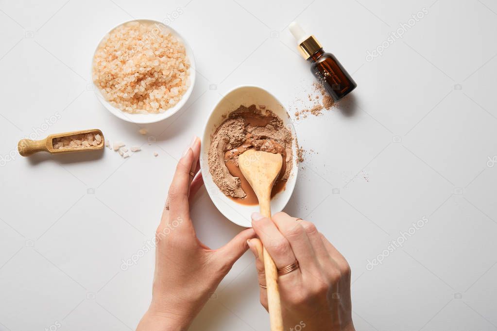 cropped view of woman mixing clay in bowl with wooden spoon near sea salt and oil on marble table