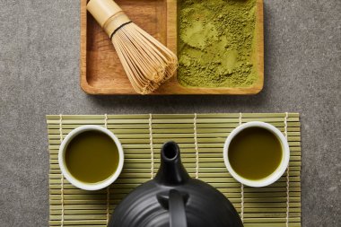 bambu çırpMa ve matcha tozu yakın yeşil masa paspas üzerinde çay ve siyah çaydanlık ile beyaz bardak üst görünümü
