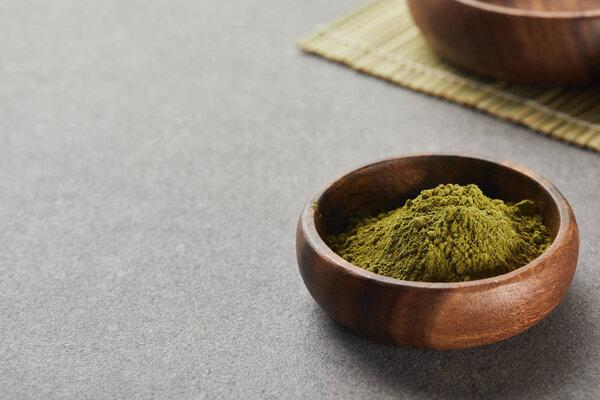 selective focus of green matcha powder in wooden bowl on grey table with copy space