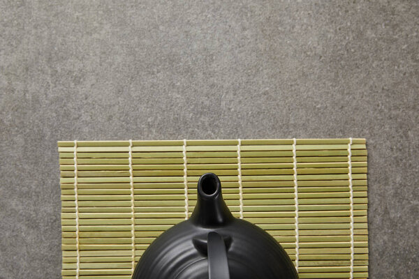 top view of green bamboo table mat with black teapot on grey surface
