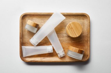 top view of few empty jars and cream tubes on wooden tray on white  clipart