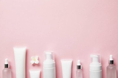 Kozmetik cam şişeleri, kremalı krema tüpleri, kozmetik kutuları ve pembe üzerine yasemin çiçeği. 