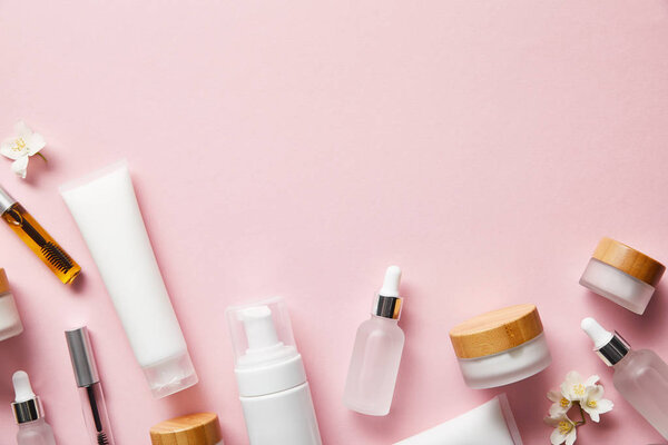 top view of cream tubes, cosmetic dispenser, empty jars and with hand cream, mascara bottles on pink 