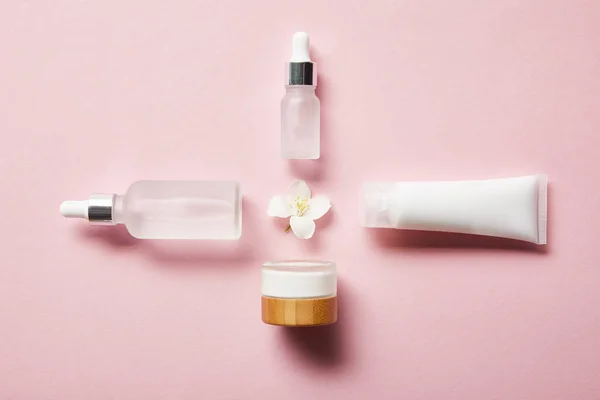 平面铺化妆品玻璃瓶 奶油管奶油和茉莉花在粉红色中间 — 图库照片