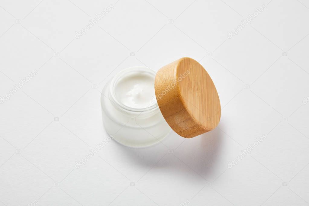 open glass jar with cream and wooden cap on white 