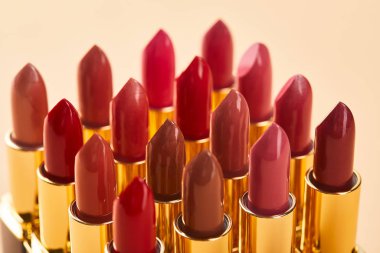 close up of various red shades of lipstick in tubes isolated on beige  clipart