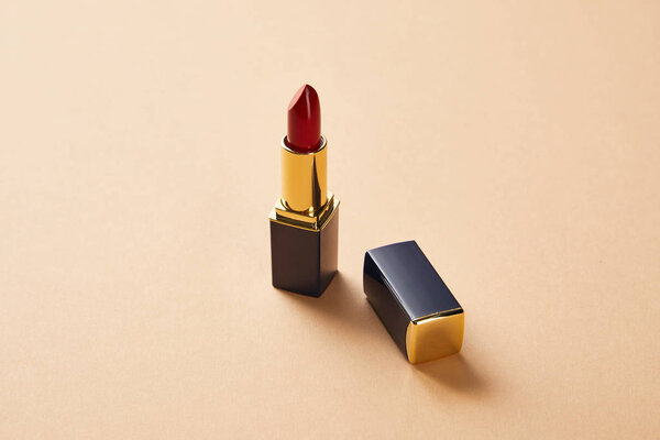 single opened tube of red lipstick on beige